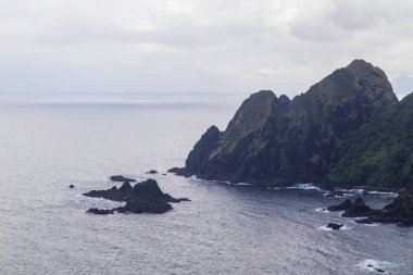 Derin mavi okyanustaki engebeli uçurumların ve volkanik kaya oluşumlarının üzerinde bulutlu bir gökyüzü..