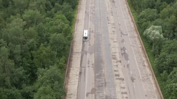 Otobanda beyaz bir otobüsle ormandan geçerken beyaz otobüsün hızı iki şeritli otoyolda ilerliyor. Yazın geniş açılı hava aracı. — Stok video