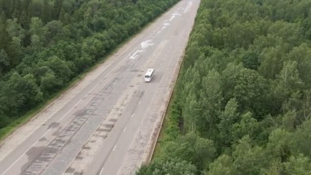 Білий автобус, що їде автобаном через ліс, швидко рухається по двосторонньому шосе. Літом широко розстріляний повітряний дрон. — стокове відео