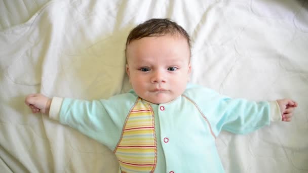 可愛い新生児の男の子の青い服は白と笑顔に横たわって — ストック動画