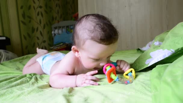 Drôle bébé tout-petit bébé garçon jouer avec son jouet, couché sur le ventre sur le lit dans la chambre — Video