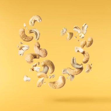 Havaya düşen taze kaju fıstıkları sarı aydınlatıcı arka planda izole edilmiş. Yiyecek uçurma konsepti. Yüksek çözünürlük.