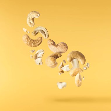 Havaya düşen taze kaju fıstıkları sarı aydınlatıcı arka planda izole edilmiş. Yiyecek uçurma konsepti. Yüksek çözünürlük.