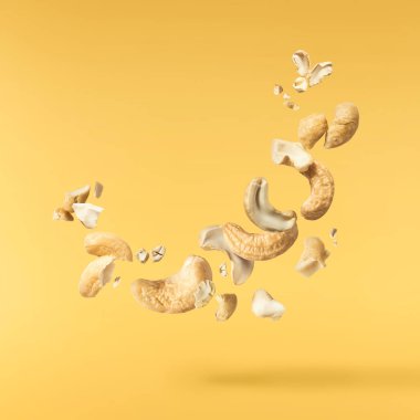 Havaya düşen taze kaju fıstıkları sarı aydınlatıcı arka planda izole edilmiş. Yiyecek uçurma konsepti. Yüksek çözünürlük.