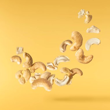 Havaya düşen taze kaju fıstıkları sarı aydınlatıcı arka planda izole edilmiş. Yiyecek uçurma konsepti. Yüksek çözünürlük.