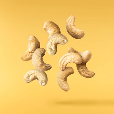 Havaya düşen taze kaju fıstıkları sarı aydınlatıcı arka planda izole edilmiş. Yiyecek uçurma konsepti. Yüksek çözünürlük.