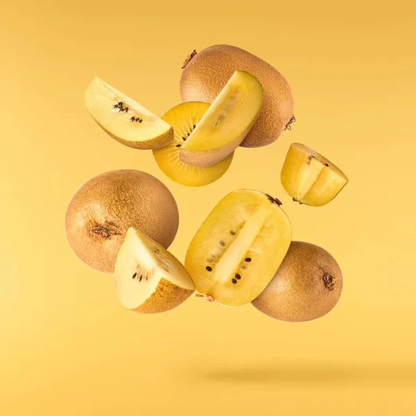 Fresh raw gold kiwi falling in the air isolated on yellow illuminating background. Food levitation concept. High resolution image