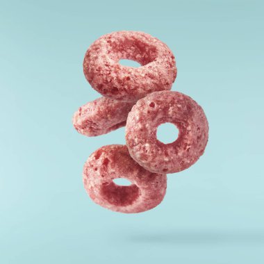 Lezzetli pembe mısır gevrekleri mavi arka planda izole bir şekilde havaya düşüyor. Gıda havalanma gebeliği. Yüksek çözünürlük