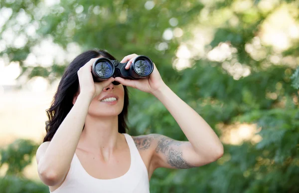 Bruna donna guardando attraverso il binocolo mentre passeggia th — Foto Stock