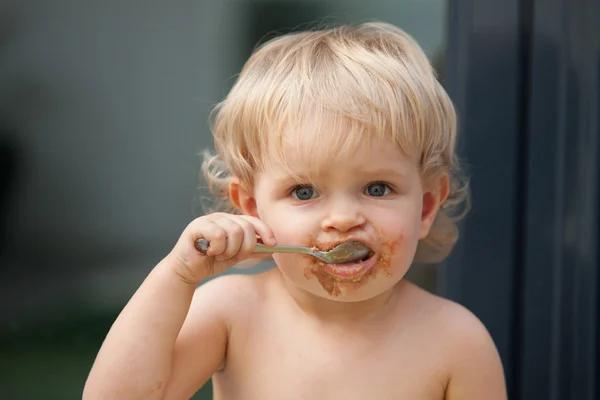 Funny blond baby eating chocolate — Stock Photo, Image