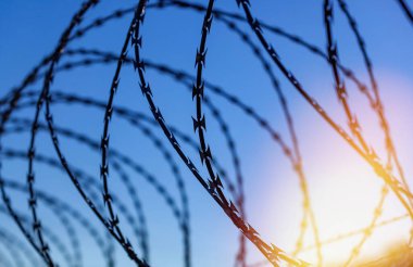 Mavi bir gökyüzünün altında dikenli telle çitle