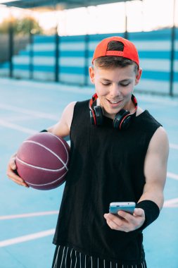 Topu olan çekici bir basketbolcu cep telefonuna bakıyor ve ara verirken gülümsüyor.