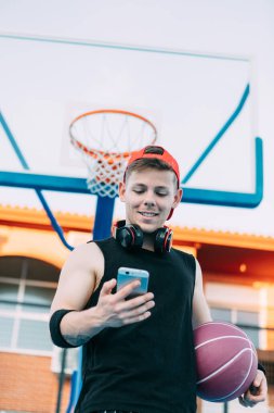 Topu olan çekici bir basketbolcu cep telefonuna bakıyor ve ara verirken gülümsüyor.
