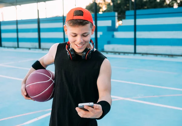 Atraktivní Chlap Basketbalista Míčem Dívá Svůj Mobilní Telefon Usmívá Při — Stock fotografie