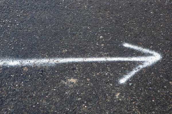 Белая стрелка, нарисованная на дороге — стоковое фото