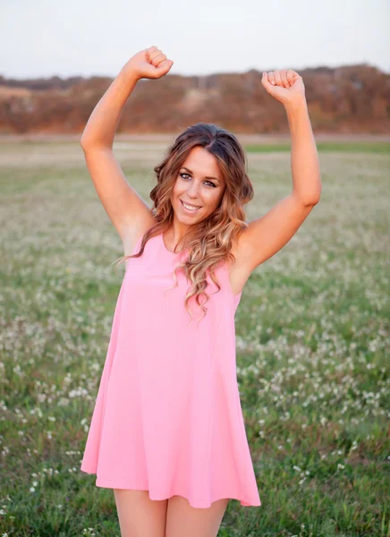 Chica con vestido rosa celebrando algo en un campo lleno de fl —  Fotos de Stock