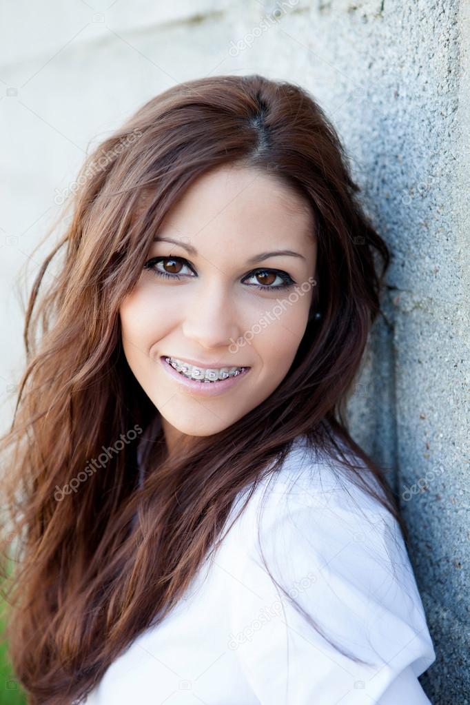 Brunette girl with brackets resting on a wall  