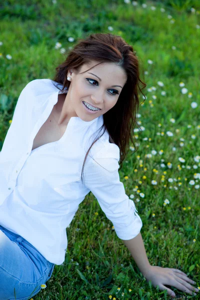 Brunette cool girl with brackets lying on the grass — Stock Photo, Image