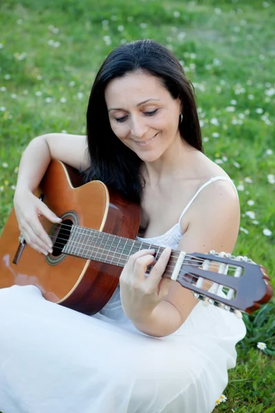 Kvinna sitter på en blomstrande äng spelar gitarr — Stockfoto