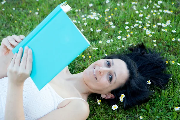 Женщина, лежащая на цветущем лугу и читающая книгу — стоковое фото