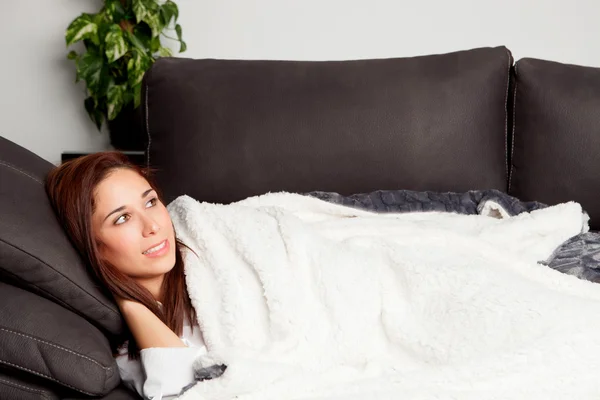 Junges Mädchen liegt auf der Couch, bedeckt mit einer Decke — Stockfoto