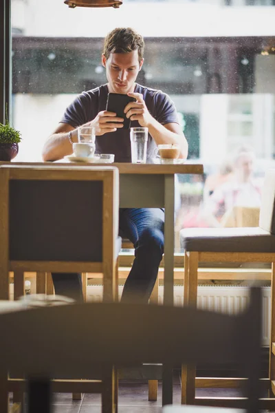 Młody człowiek ogląda tabletki w kawiarni — Zdjęcie stockowe