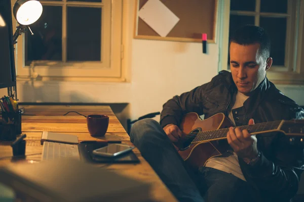 Han spiller gitar hjemme etter jobben. – stockfoto