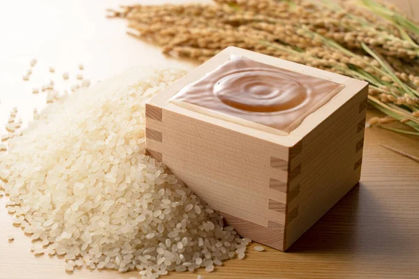 酒の入った四角い箱 酒を一滴 リップル 背景にある米と米の耳 — ストック写真