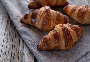 Eski ahşap bir arka plana yerleştirilmiş bir kumaş üzerindeki kruvasan. Kahvaltı resimleri