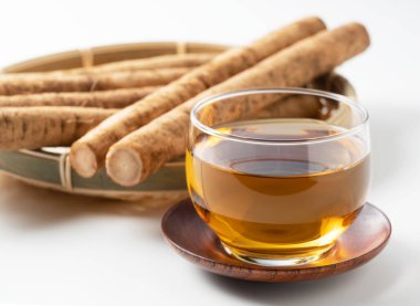 Beyaz arka planda burdock çayı. Arkasında çiğ bir dulavrat var.