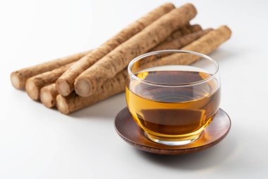 Beyaz arka planda burdock çayı. Arkasında çiğ bir dulavrat var.
