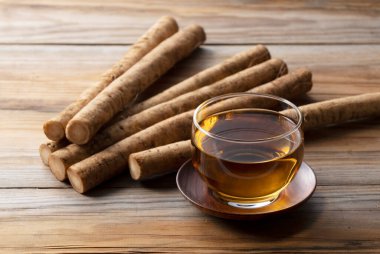 Ahşap bir arka plana yerleştirilmiş burdock çayı. Arkasında çiğ bir dulavrat var.