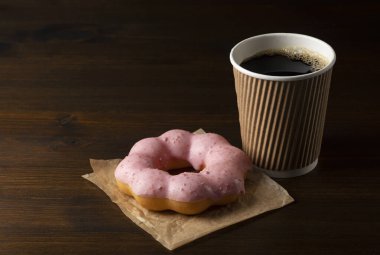 Koyu ahşap arka planda pembe çöreklerle dolu kağıt bardakta sıcak kahve.