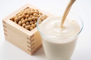 Pour soy milk into a glass placed on a white background. Soybeans in a Masu in the background clipart