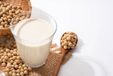 Bardakta soya sütü ve soya fasulyesi ve fotokopi alanı olan beyaz bir arka planda tahta kaşık.