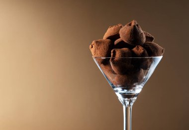 Kahverengi gradyan arkaplan üzerinde bir kokteyl bardağındaki çikolata trüf mantarları.