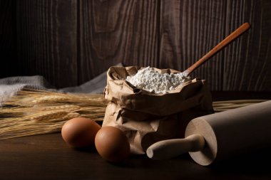 Koyu ahşap zemin üzerine un konmuş. Yumurta, merdane ve buğday kulakları kullanarak kavram.