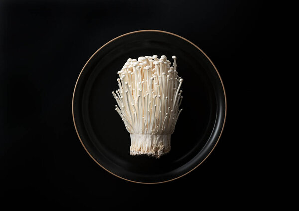 Enoki mushrooms in a plate set against a black background. View from above.