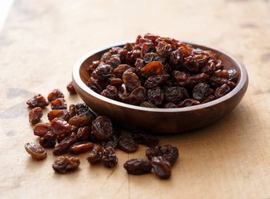 Raisins in a wooden bowl set against an old wooden background.