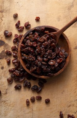 Raisins in a wooden bowl set against an old wooden background. View from directly above.
