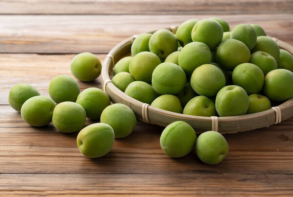 Незрелые сливы в бамбуковом дуршлаге помещены на деревянном фоне. Японский абрикос.