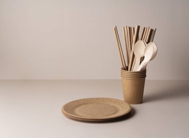 Kahverengi kağıt bardaklar, pipetler, kaşıklar ve plakalar bej arka planda. Sıfır atık kavramı. 