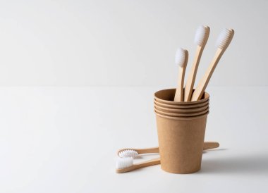 Kahverengi kağıt bardaklar ve beyaz arka planda bambu diş fırçaları. Sıfır atık kavramı. 