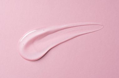 Pembe arka planda şeffaf jel damlası. Sıvı jel kozmetik leke dokusu. Güzellik serumu düştü. Şeffaf cilt bakım ürünü örneği.