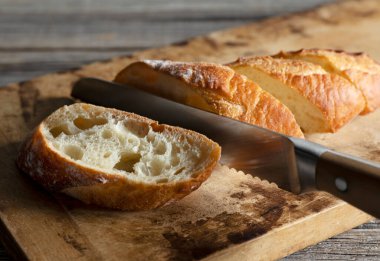 Bir ekmeği bıçakla kesmek, eski bir tahta kesme tahtasına yerleştirmek. Yakın plan..