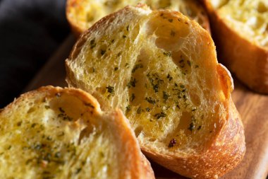 Masadaki tahta kesme tahtasının üzerinde sarımsaklı ve otlu dilimlenmiş ekmek. Yakın plan..