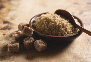 Tahta bir çanakta esmer şeker eski bir ahşap arka planda, yanında şeker küpü..