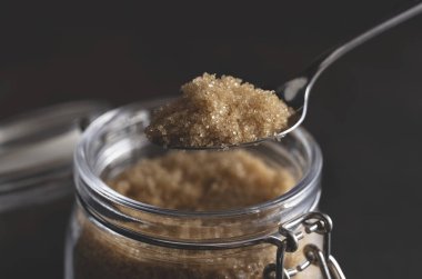 Kaşık gibi esmer şekeri siyah taştan bir arka planda duran cam bir kabın içine koyuyor..