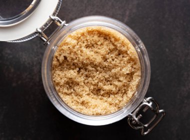 Siyah taştan bir arka planda duran cam bir kabın içindeki esmer şeker. Doğrudan yukarıdan görüntüle.