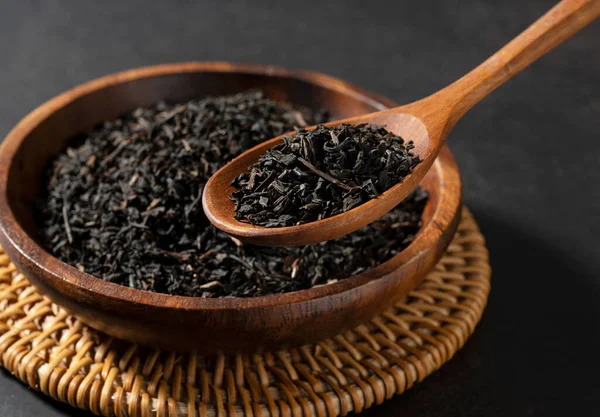 茶叶放在木制的盘子里 勺子放在黑色的背景上 采摘茶叶并托起它们 — 图库照片